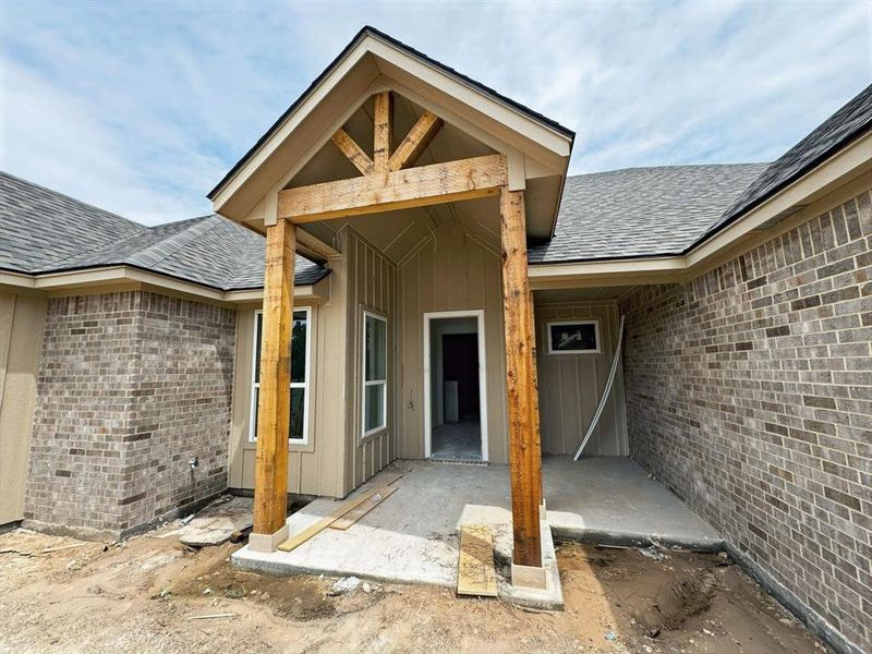 Doorway to property featuring a shingled roof, brick siding, a patio area, and board and batten siding
