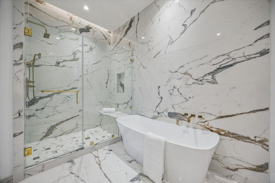 A freestanding soaking tub serves as the centerpiece, paired with a sleek glass-enclosed shower featuring designer fixtures & a built-in bench—creating a luxurious space for both relaxation & everyday comfort.