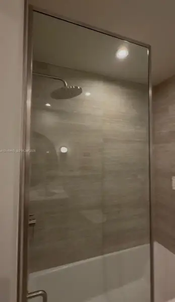 Shower featuring a stainless steel rainfall showerhead, glass enclosure with a metallic frame, and horizontal tile wall surfacing