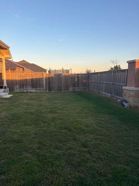 The property features a spacious lawn area, enclosed by a wooden fence