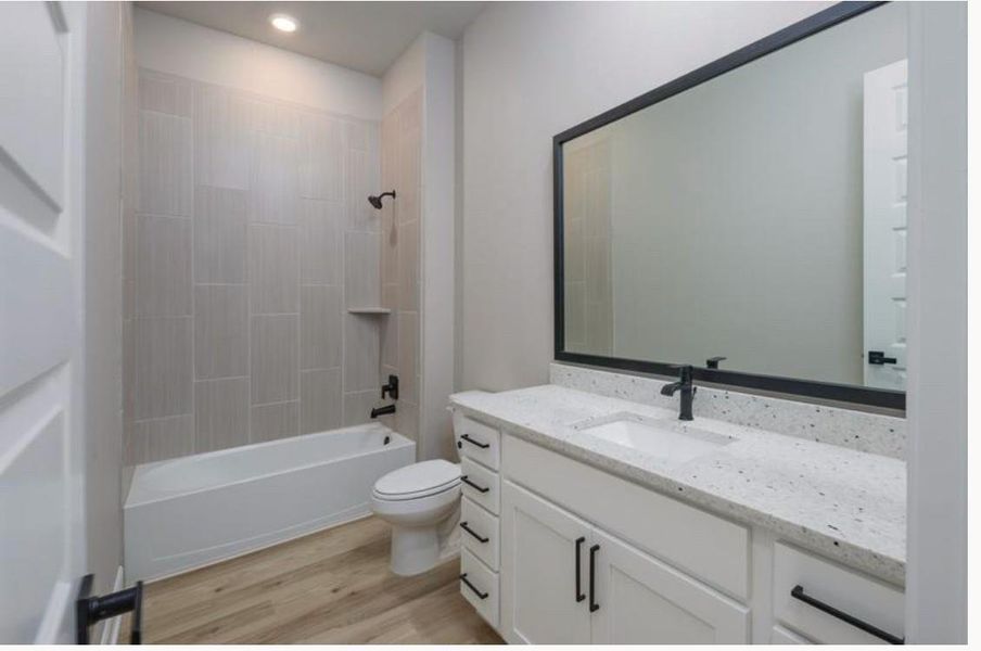 This modern bathroom boasts a sleek tub and shower combo, light wood flooring, and a spacious vanity with a large mirror. White cabinetry and neutral tones create a clean, inviting space.