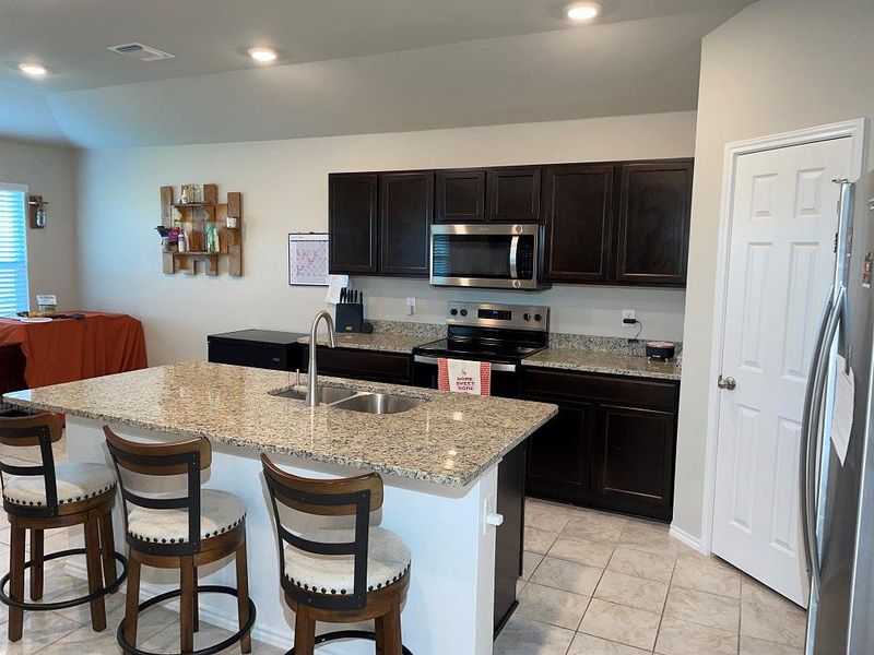 Kitchen featuring appliances with stainless steel finishes, a center island with sink, light stone counters, a kitchen breakfast bar, and recessed lighting
