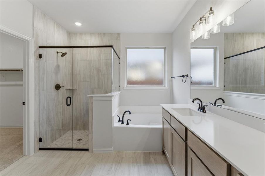 Spacious bathroom featuring a frameless glass shower enclosure with matte black hardware, a built-in soaking tub, dual vanity with undermount sinks and quartz countertop, and wood-finish tile flooring