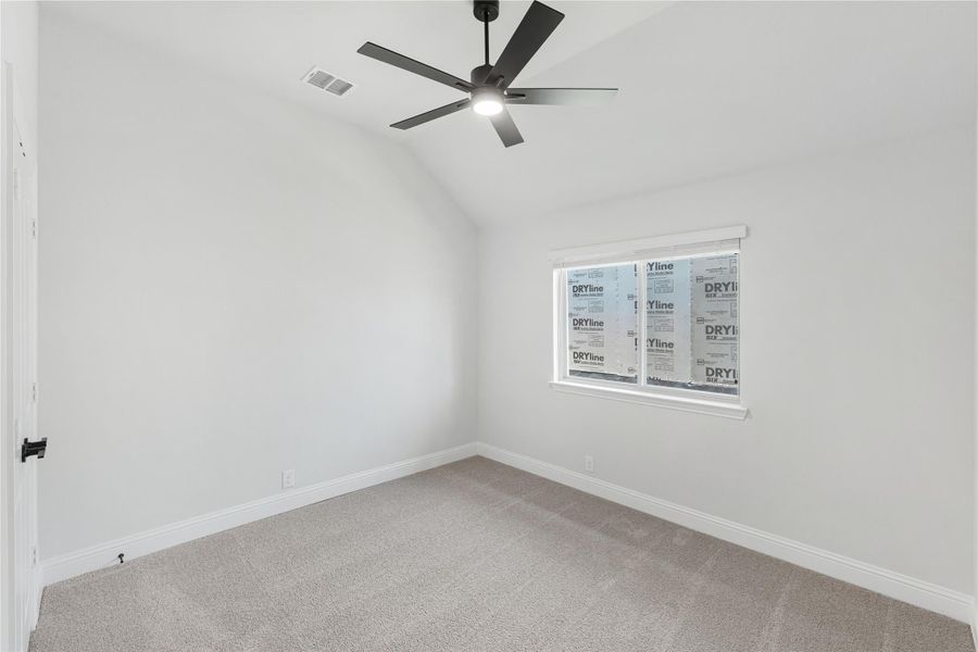 Empty bedroom with vaulted ceiling, black ceiling fan, carpet flooring, and a single window under construction.