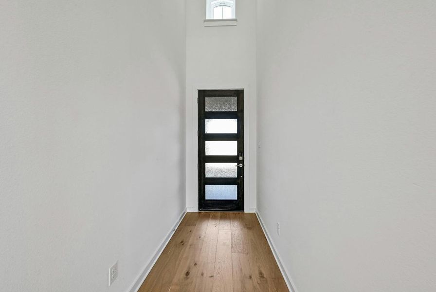 Doorway to outside featuring light wood finished floors and a towering ceiling