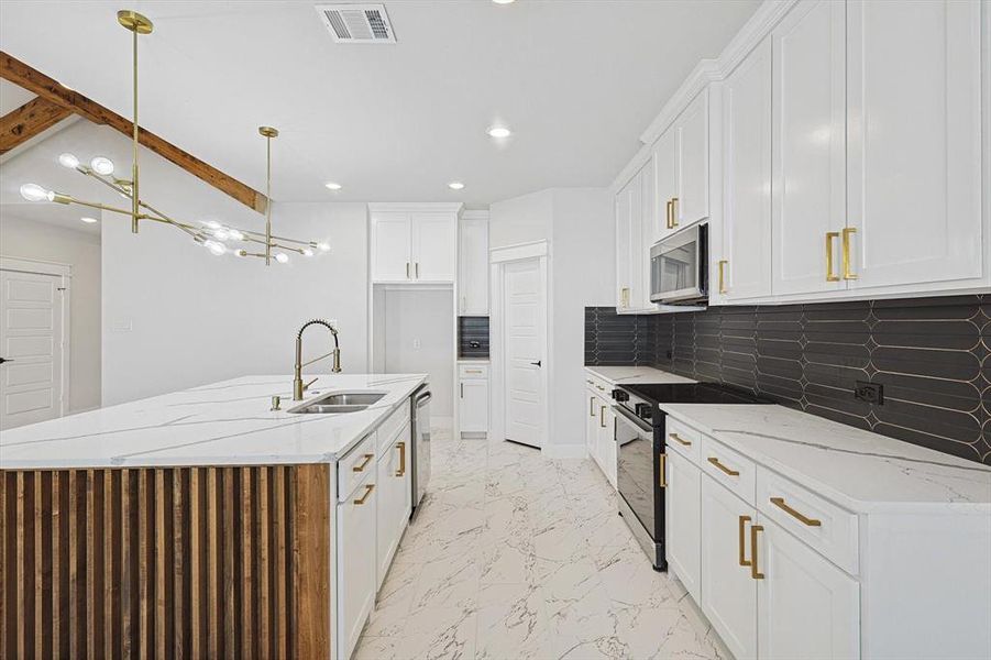 Kitchen featuring pendant lighting, white cabinetry, sink, stainless steel appliances, and a center island with sink