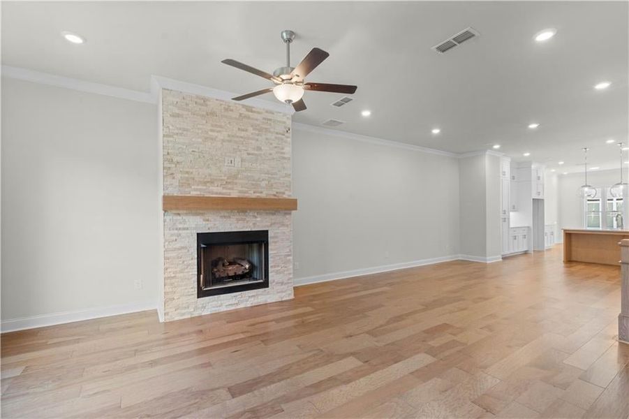 Unfurnished living room featuring a stone fireplace, light wood-type flooring, ornamental molding, recessed lighting, and ceiling fan