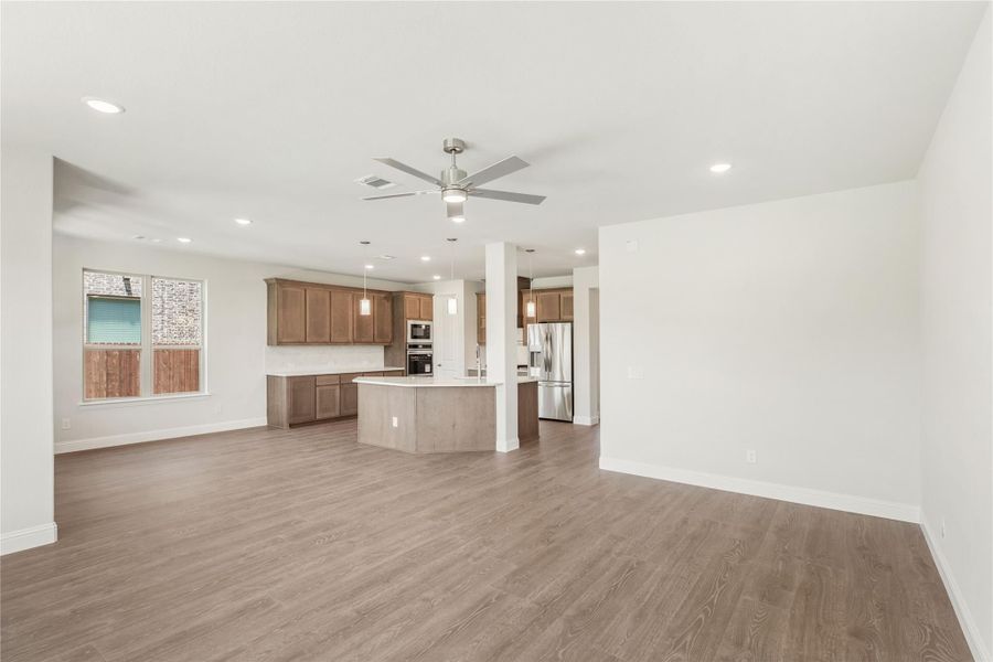 Open living area with hardwood floors and ceiling fan flowing into kitchen with island and stainless appliances