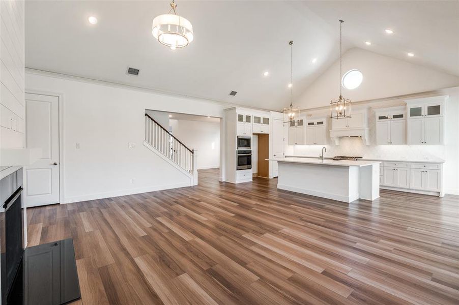 Large living room with high vaulted ceiling, dark wood finished floors, stairs, a chandelier, and a fireplace Large living room with high vaulted ceiling, dark wood finished floors, stairs, a chandelier, and a fireplace