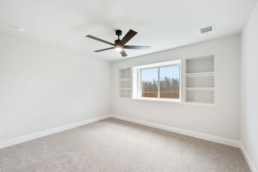 Empty bedroom with carpet, ceiling fan, and built-in wall shelves flanking a window