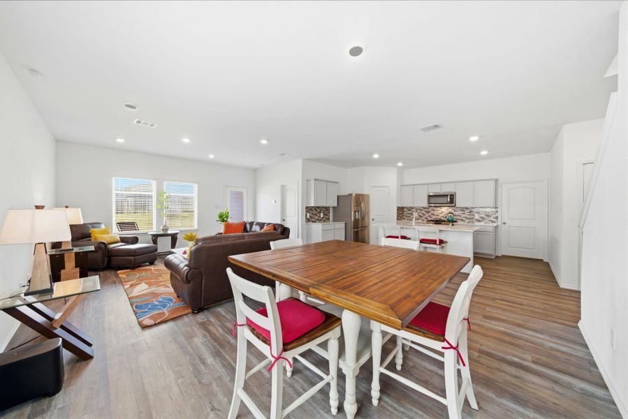 Wide, integrated view from dining through the kitchen to the living room. Modern, open, and inviting.