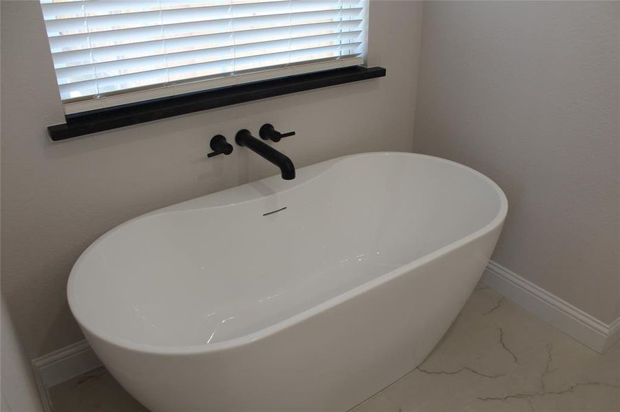 Full bathroom with marble finish floors, a soaking tub, and baseboards Full bathroom with marble finish floors, a soaking tub, and baseboards