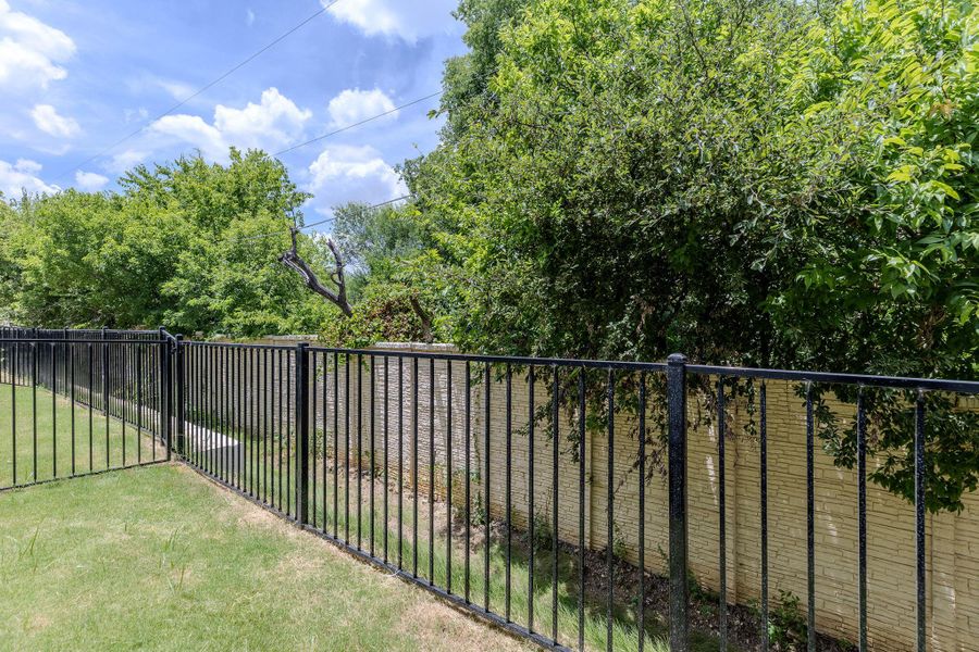 Secure yard featuring a durable black wrought iron fence and mature landscaping for optimal privacy.