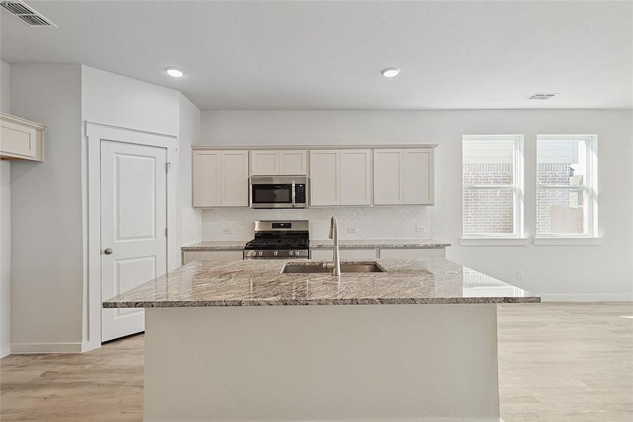 Kitchen featuring a kitchen island with sink, stainless steel appliances, sink, light stone countertops, and light wood-type flooring