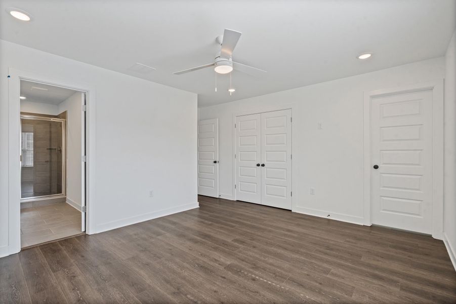 Wood-finish flooring with recessed lighting, a ceiling fan, a shower enclosure with a glass door, and white paneled interior doors Wood-finish flooring with recessed lighting, a ceiling fan, a shower enclosure with a glass door, and white paneled interior doors