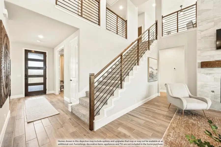 Two-story entryway with carpeted staircase, wood railing, front door, and light wood-look tile floors