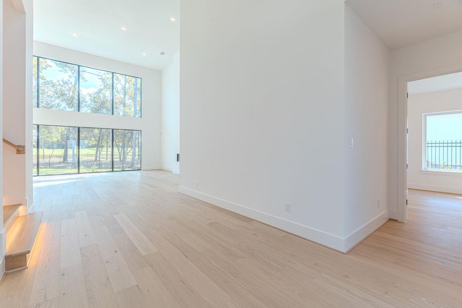 This home features a spacious, modern living area with high ceilings and abundant natural light from large windows. The light wood flooring and open layout create an inviting and airy atmosphere.