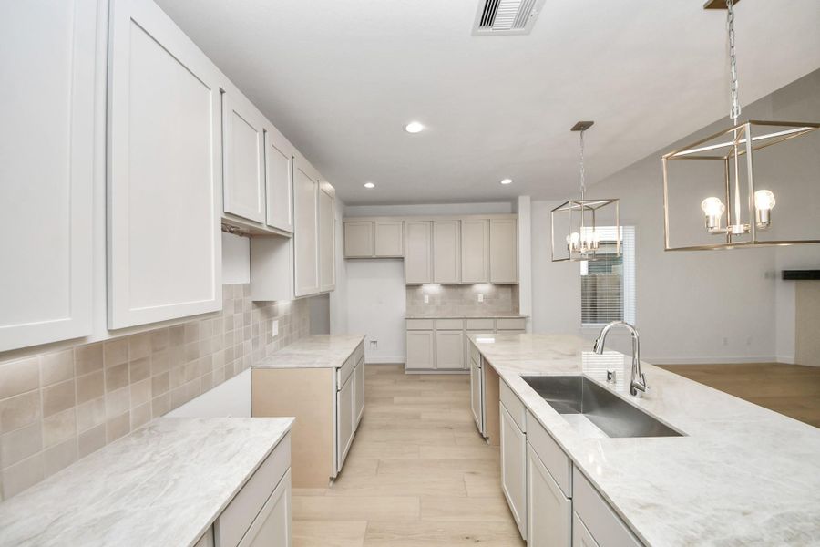 This kitchen is truly a chef's dream! This haven Boasts high ceilings, recessed & pendant lighting, stained wood cabinets, granite countertops, stainless steel appliances, a modern tile backsplash.  All of this overlooks your expansive family room, creating a perfect space for culinary delights and family gatherings. Sample photo of completed home with similar floor plan. Actual colors and selections may vary.