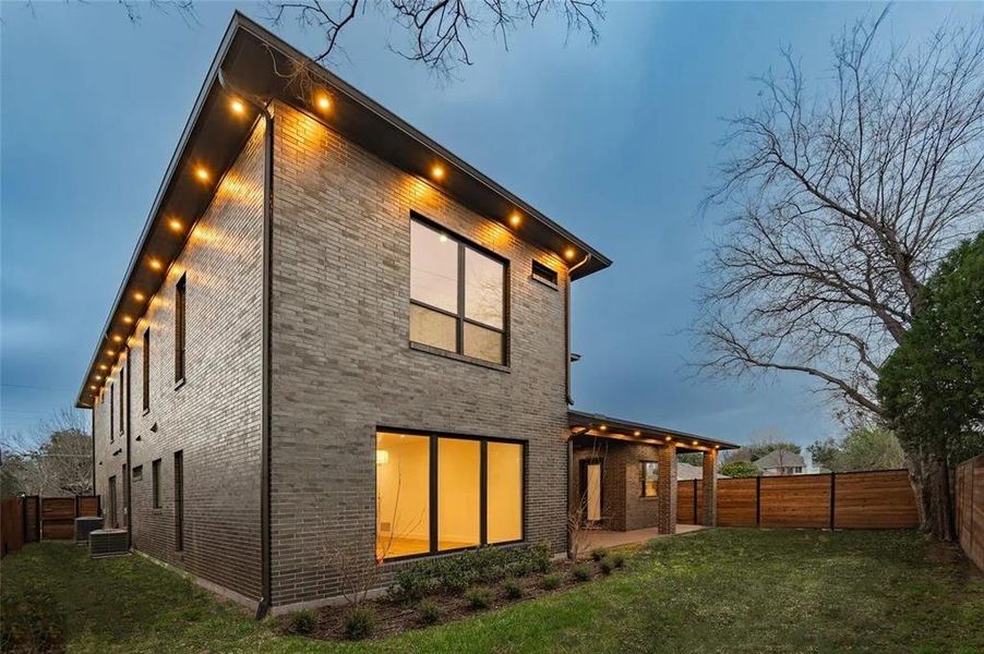 Contemporary brick exterior with large windows, recessed soffit lighting, a covered patio, and wood fencing Contemporary brick exterior with large windows, recessed soffit lighting, a covered patio, and wood fencing