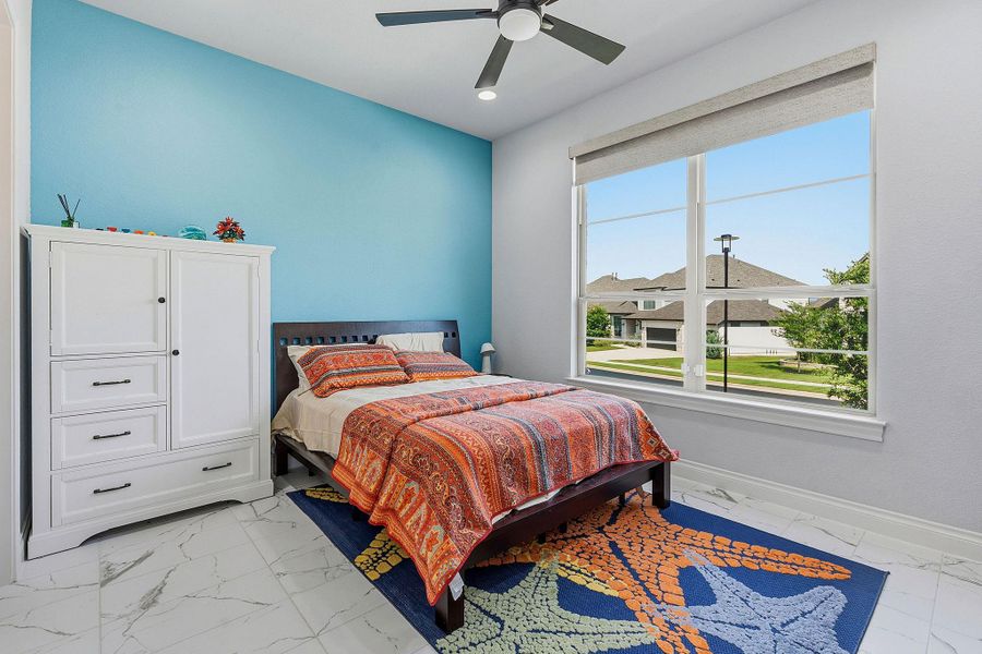 A cheerful bedroom space, complete with a ceiling fan for comfort and an expansive window illuminating the interior. A cheerful bedroom space, complete with a ceiling fan for comfort and an expansive window illuminating the interior.