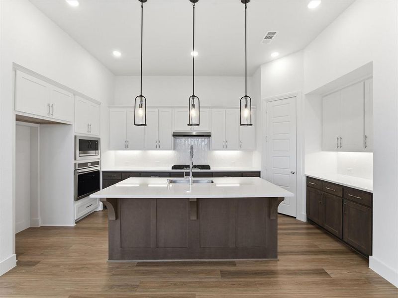 Kitchen with a kitchen breakfast bar, an island with sink, two tone color scheme, stainless steel appliances, and pendant lighting