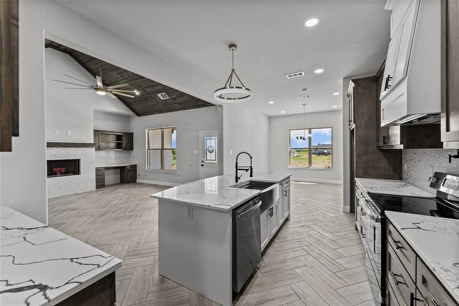 Kitchen with stainless steel appliances, decorative light fixtures, light stone counters, tasteful backsplash, and a center island with sink Kitchen with stainless steel appliances, decorative light fixtures, light stone counters, tasteful backsplash, and a center island with sink