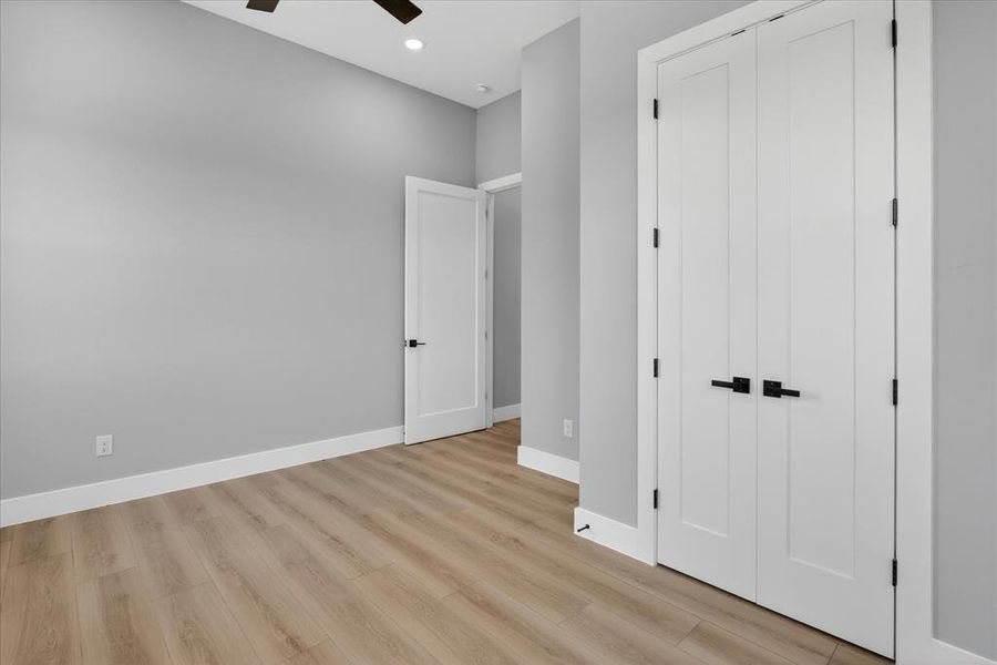 Room featuring light gray walls, wood-finish flooring, white baseboards, and a ceiling fan