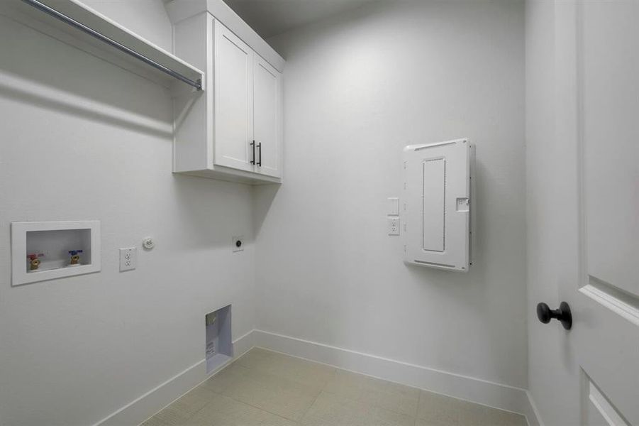 Dedicated laundry area featuring a hanging rod, overhead cabinetry with dark hardware, and tile flooring Dedicated laundry area featuring a hanging rod, overhead cabinetry with dark hardware, and tile flooring