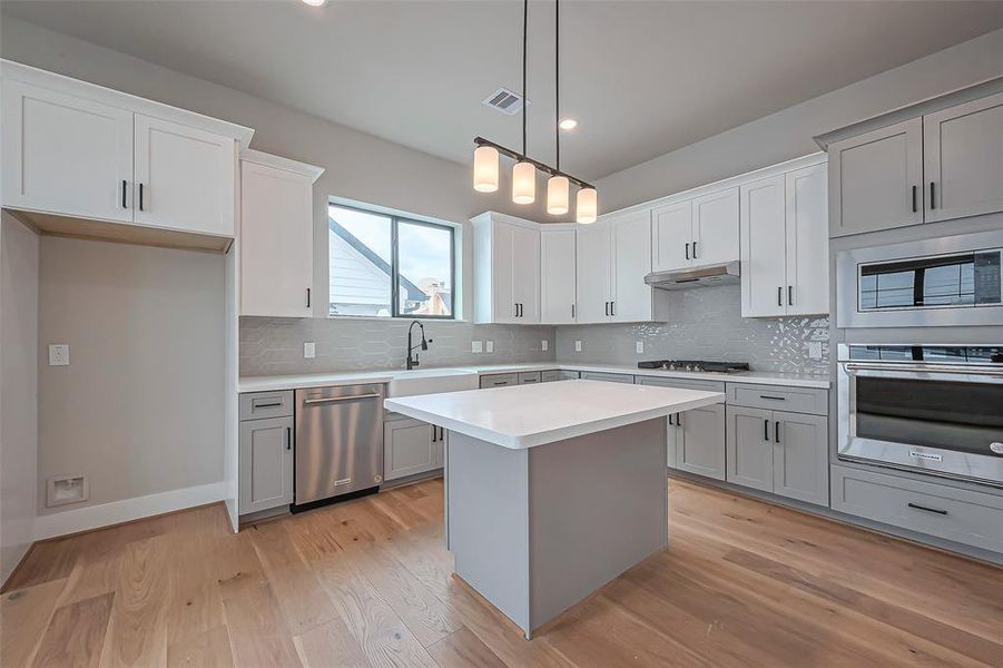 Discover a modern kitchen with sleek white cabinetry, a stylish tile backsplash, and a spacious island with pendant lighting. The open layout seamlessly extends into a bright living area with hardwood floors and a contemporary staircase.