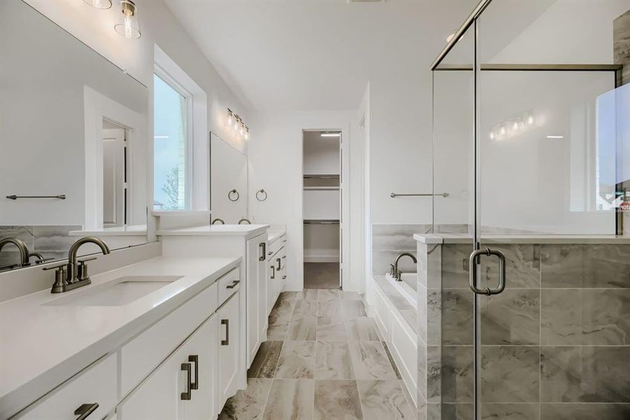 Full bathroom featuring two vanities, a shower stall, a bath, a spacious closet, and light marble finish flooring