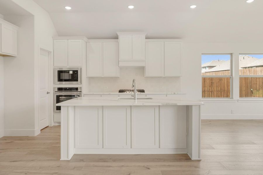 White kitchen with large center island, white cabinets, stainless steel appliances, and light wood floors