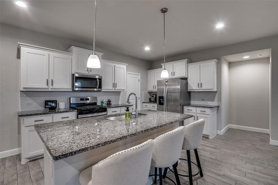 Kitchen with a kitchen breakfast bar, light wood-style floors, backsplash, stainless steel appliances, and white cabinetry
