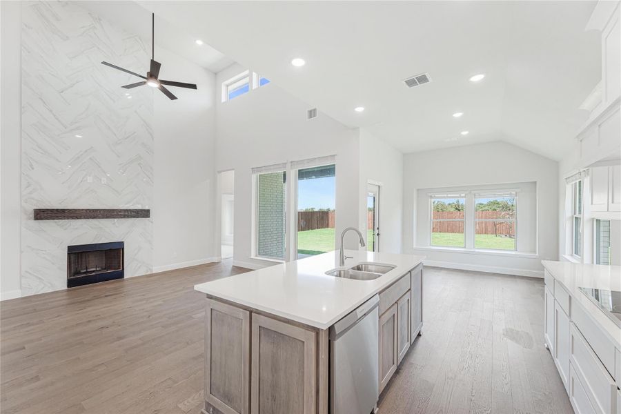 Open-concept kitchen with center island, sink, and view of living room with marble tile fireplace and vaulted ceiling
