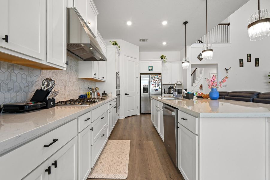 White cabinetry and stone countertops frame this open kitchen featuring a central island and wood flooring.