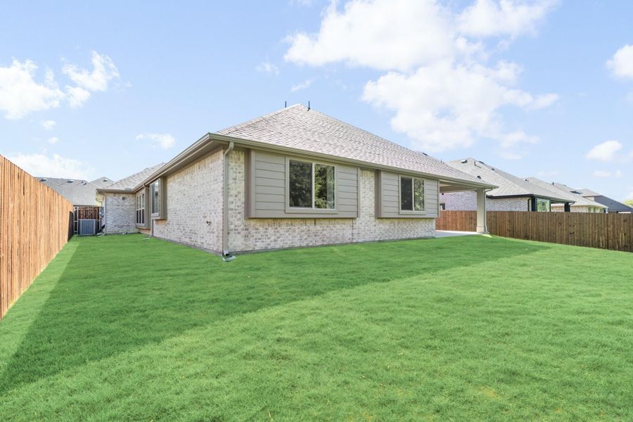 Rear exterior of single-story brick home with large fenced backyard and green lawn