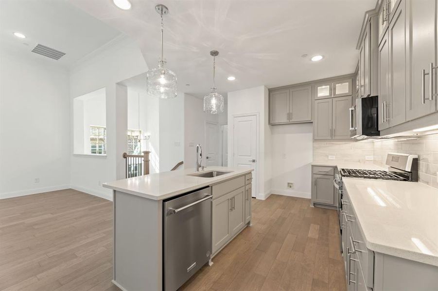 Kitchen with sink, an island with sink, stainless steel appliances, decorative light fixtures, and light hardwood / wood-style flooring