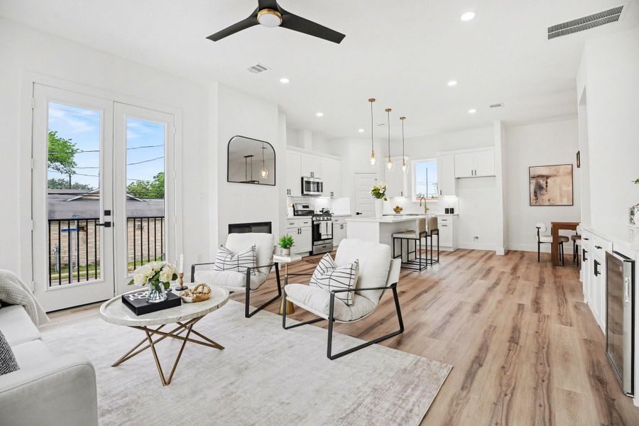 This modern open-concept living area features a sleek kitchen with an island and pendant lighting, a cozy seating area with a fireplace, and large windows providing ample natural light. The space is accented with light wood flooring and contemporary decor, creating a welcoming and stylish atmosphere.