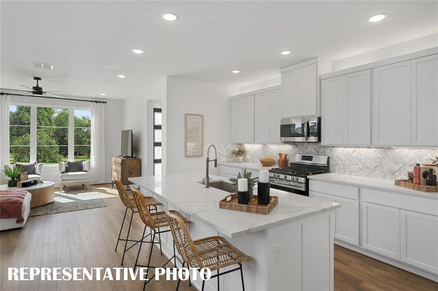 Kitchen featuring cabinetry, backsplash, light stone counters, stainless steel appliances, and a center island with sink