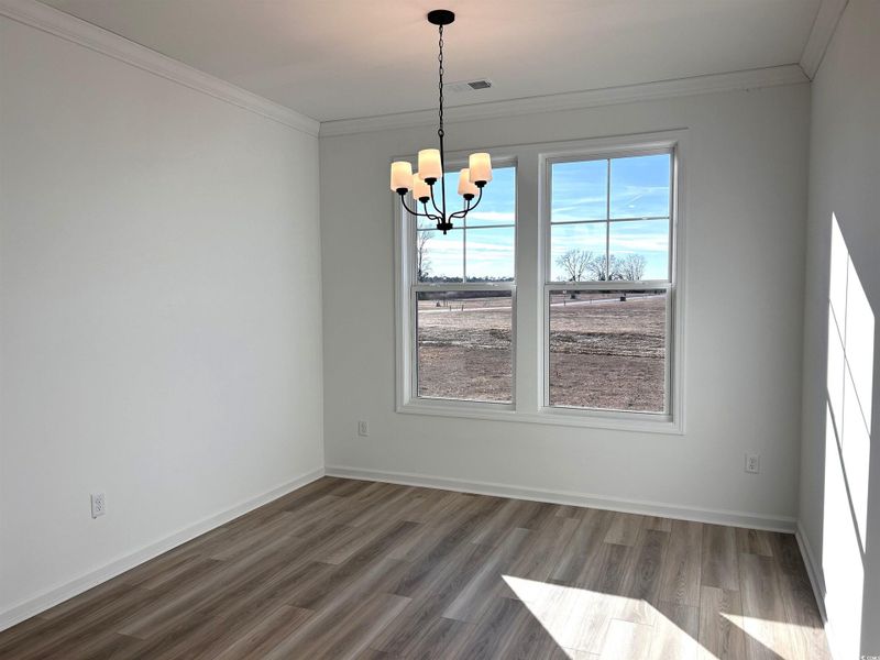 Unfurnished dining area with wood finished floors, crown molding, and a chandelier