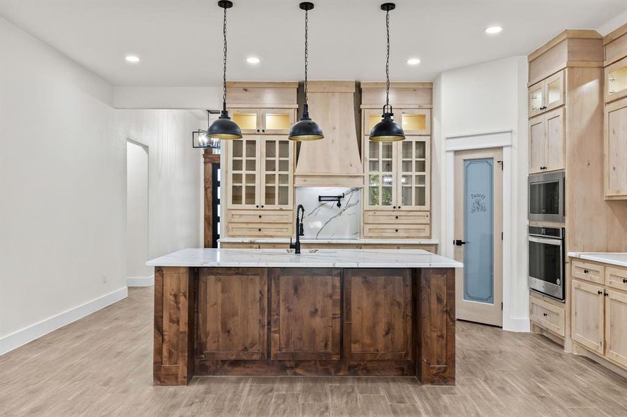 Kitchen with light brown cabinets, glass insert cabinets, light stone countertops, stainless steel appliances, and light wood-type flooring