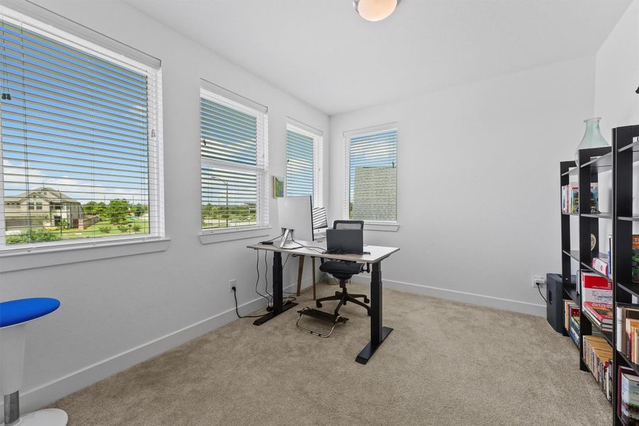 This versatile room is currently being used as a second home office, offering a private and sunlit workspace. The room has stunning views of the nearby amenity area and the main entrance to the community.