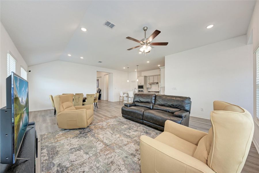 Bright and inviting living area features a high ceiling and recessed lighting, flowing seamlessly into the dining and kitchen spaces.