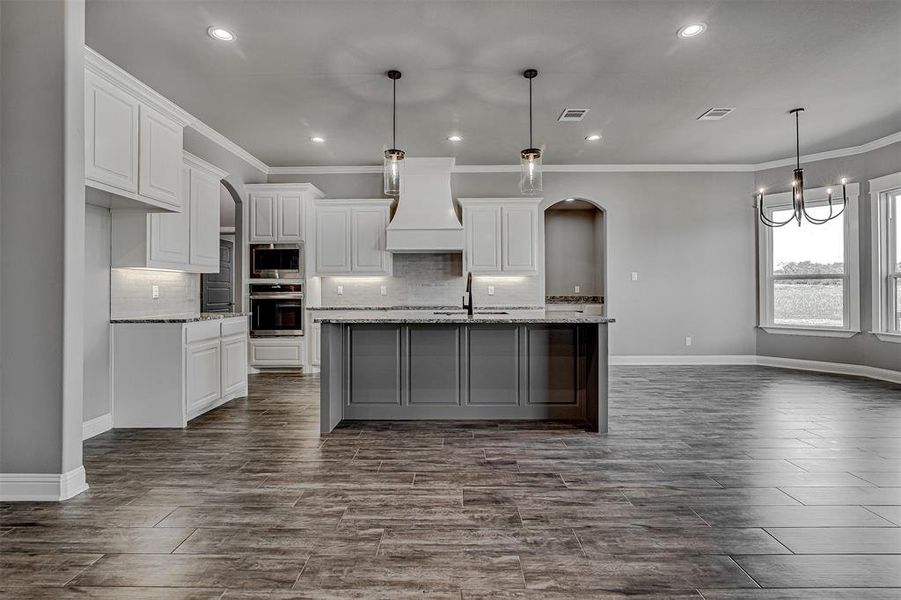 Kitchen featuring stainless steel appliances, an island with sink, white cabinetry, and custom range hood