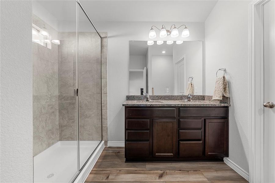 Bathroom with double vanity, a stall shower, and light wood-type flooring
