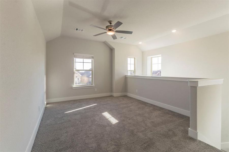 Unfurnished room with carpet floors, vaulted ceiling, healthy amount of natural light, and ceiling fan