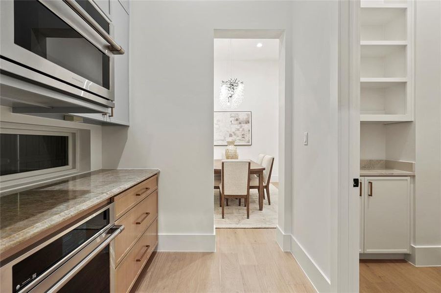 Kitchen featuring appliances with stainless steel finishes, light stone counters, light wood finished floors, and decorative light fixtures
