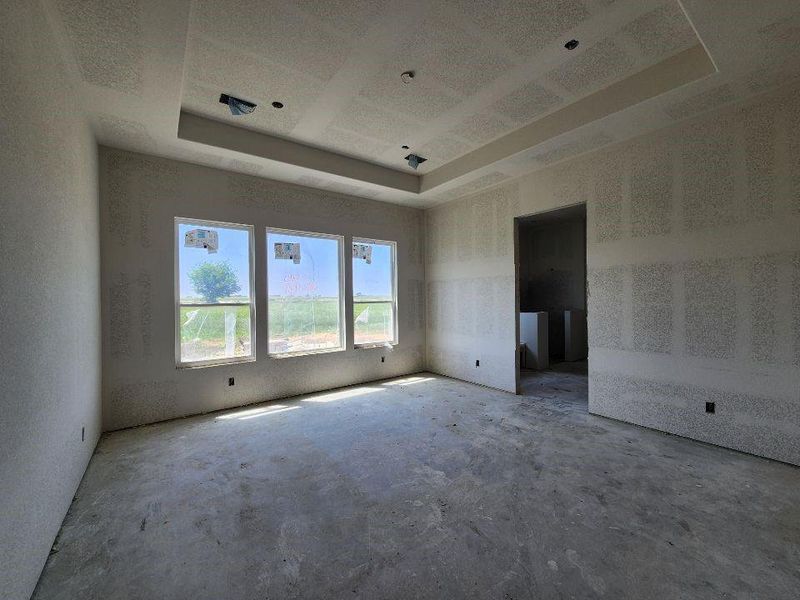 Room under construction featuring an architectural tray ceiling with recessed lighting provisions, three large windows, an open doorway, and a concrete subfloor