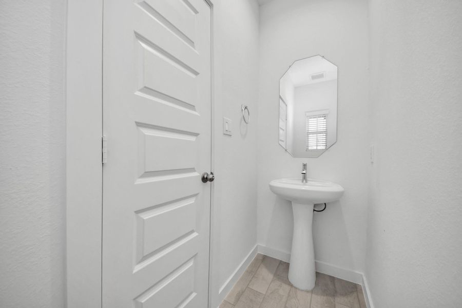 This half bathroom features a stylish pedestal sink, modern hardware, and bright recessed lighting, creating a sleek and inviting space. Sample photo of completed home with similar floor plan. Actual colors and selections may vary.