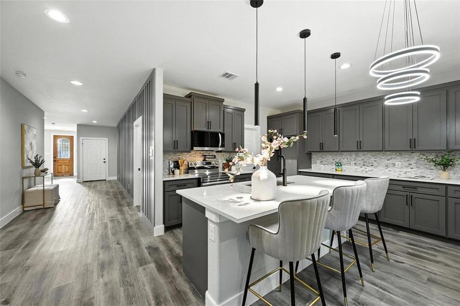 Kitchen with a kitchen breakfast bar, a center island with sink, wood finished floors, decorative backsplash, and stainless steel appliances Kitchen with a kitchen breakfast bar, a center island with sink, wood finished floors, decorative backsplash, and stainless steel appliances