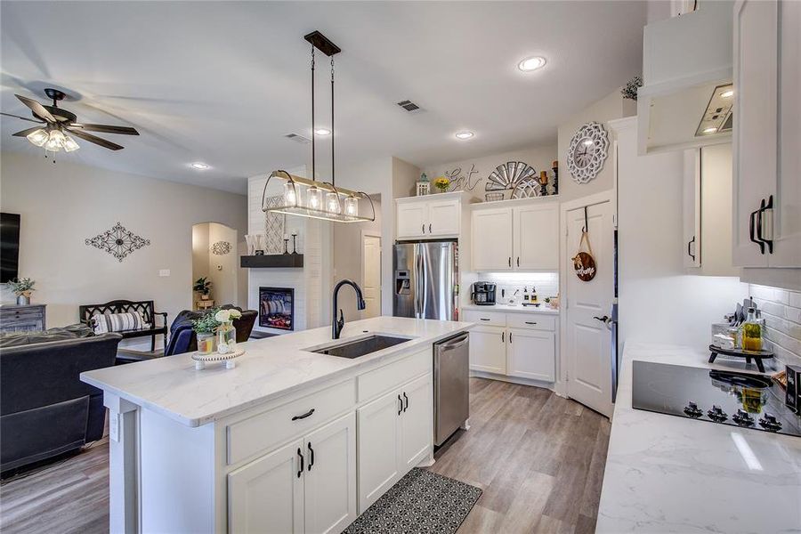 Kitchen with white cabinetry, sink, hanging light fixtures, a center island with sink, and appliances with stainless steel finishes